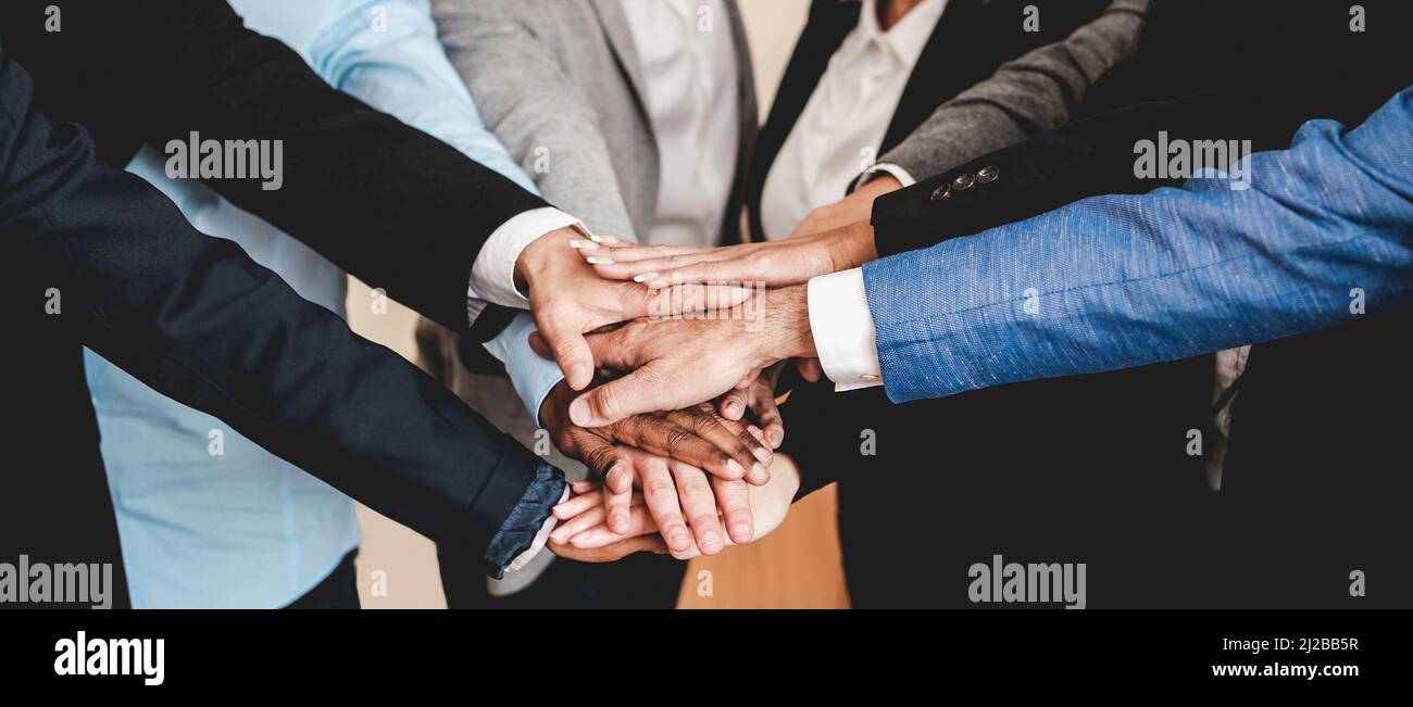 Uomini d'affari multiculturali che si accatastano le mani con i colleghi all'interno di uffici moderni - Focus on African man hands Foto Stock