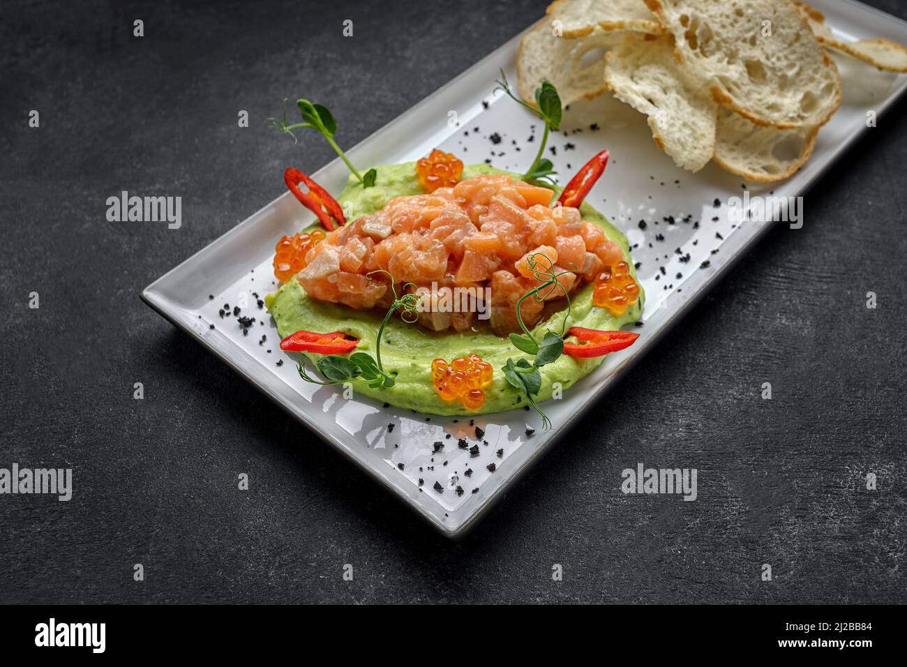 Tartare di salmone con purea di avocado rosso, caviale e crostini. Su un piatto, su sfondo scuro Foto Stock