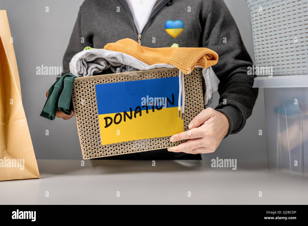 Casella di partecipazione volontaria con aiuto per il popolo ucraino. Confezione con bandiera Ucraina con abiti usati per la donazione. Aiuto umanitario all'Ucraina primo piano Foto Stock