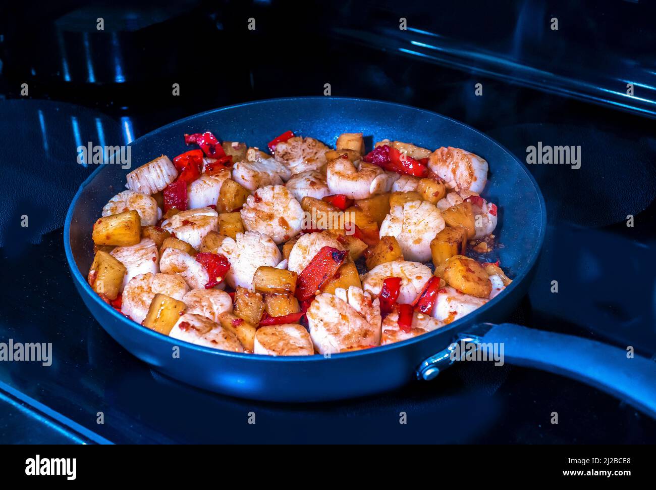 Cena in padella con capesante, ananas e peperoni rossi cucinati in padella su una stovetop Foto Stock