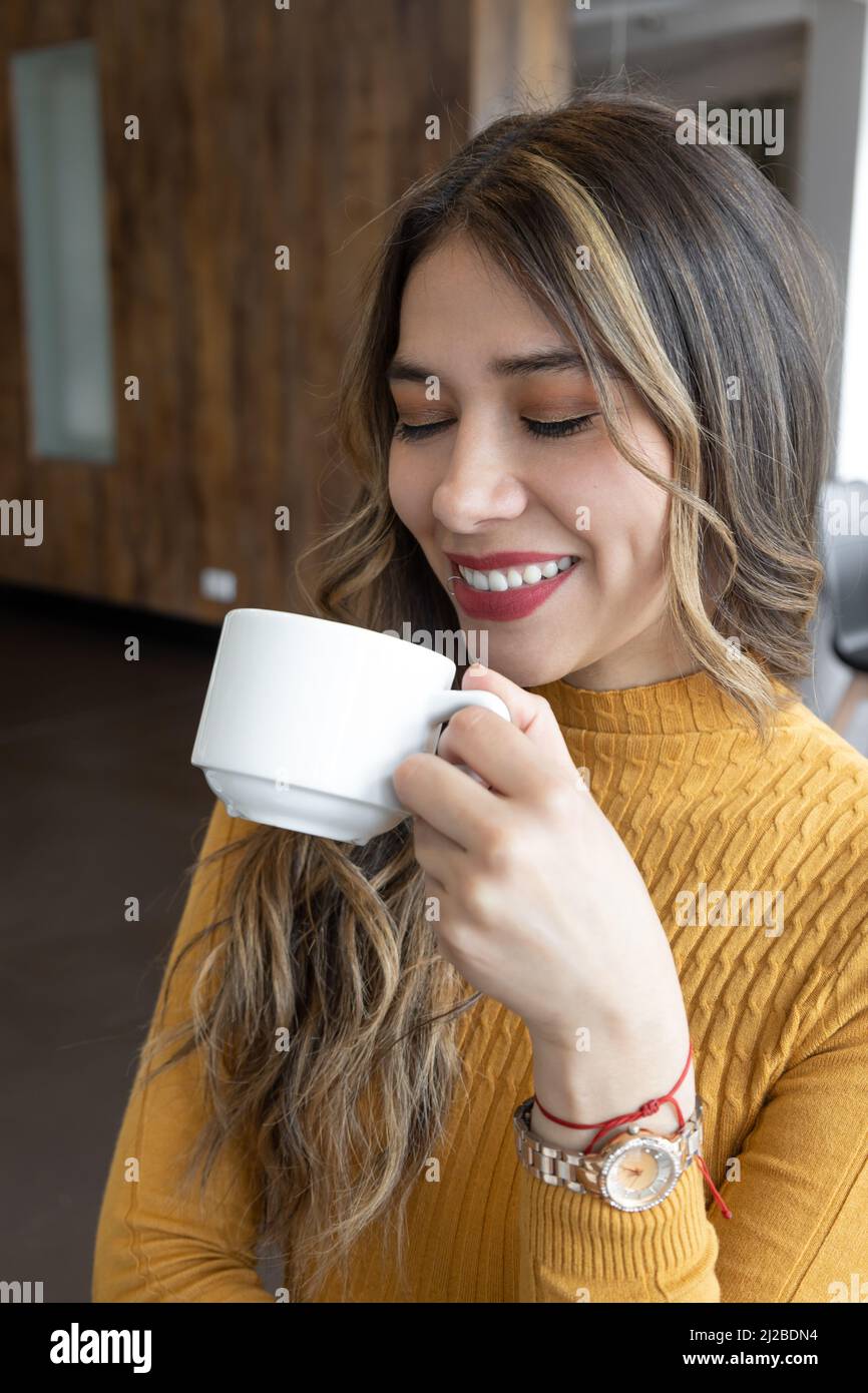 donna latina con lunghi capelli biondi sorridenti, tazza con bevanda calda, stile di vita, trucco e colazione al caffè Foto Stock