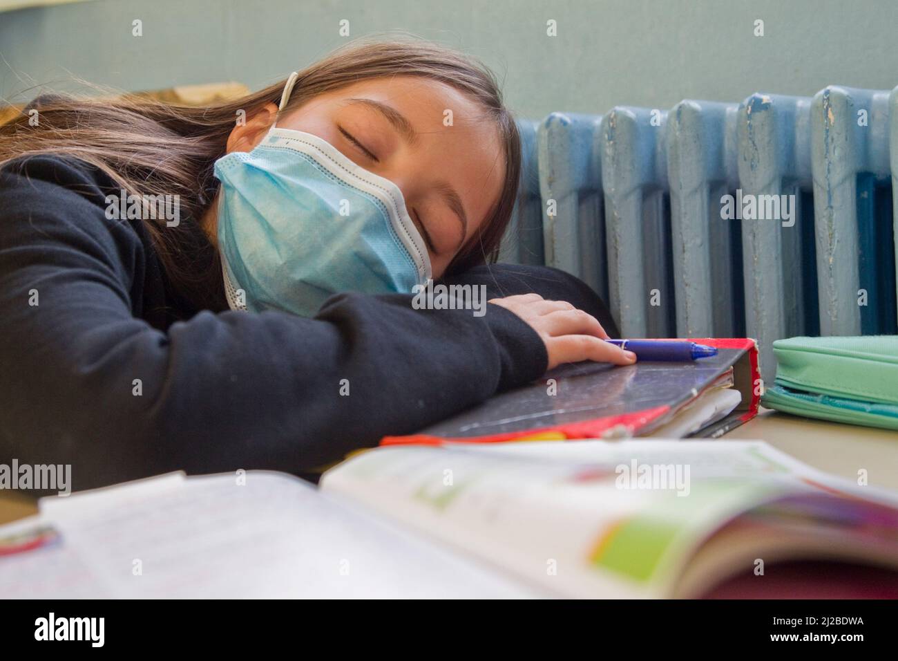 Scuola elementare durante il Covid-19, Coronavirus focolaio: Scolarella con una maschera viso addormentato in una classe Foto Stock