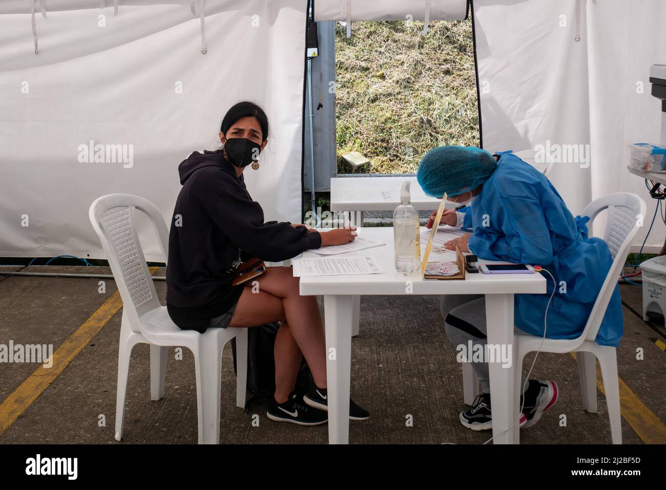 Rionegro, Antioquia, Colombia - Dicembre 19 2021: Personale sanitario con una Donna dai capelli scuri che compila un modulo con i suoi dati per prendere il Test PCR in O. Foto Stock