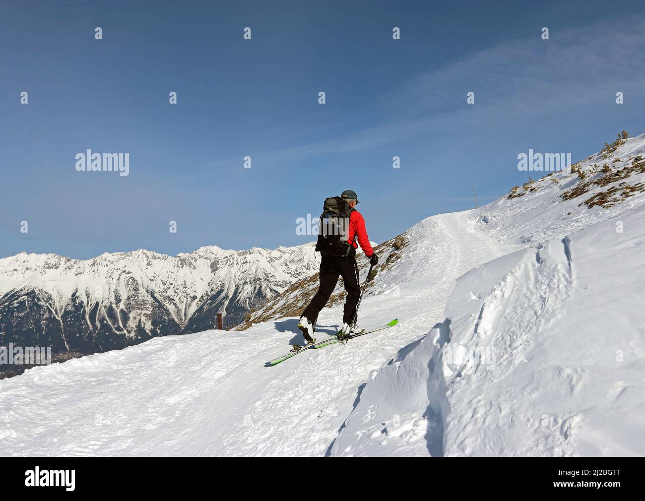 Immagine generica di un uomo che porta zaino e pali che cammina su una montagna innevata con sci contro un cielo blu (Patscherkofel, Alpi, Austria) Foto Stock