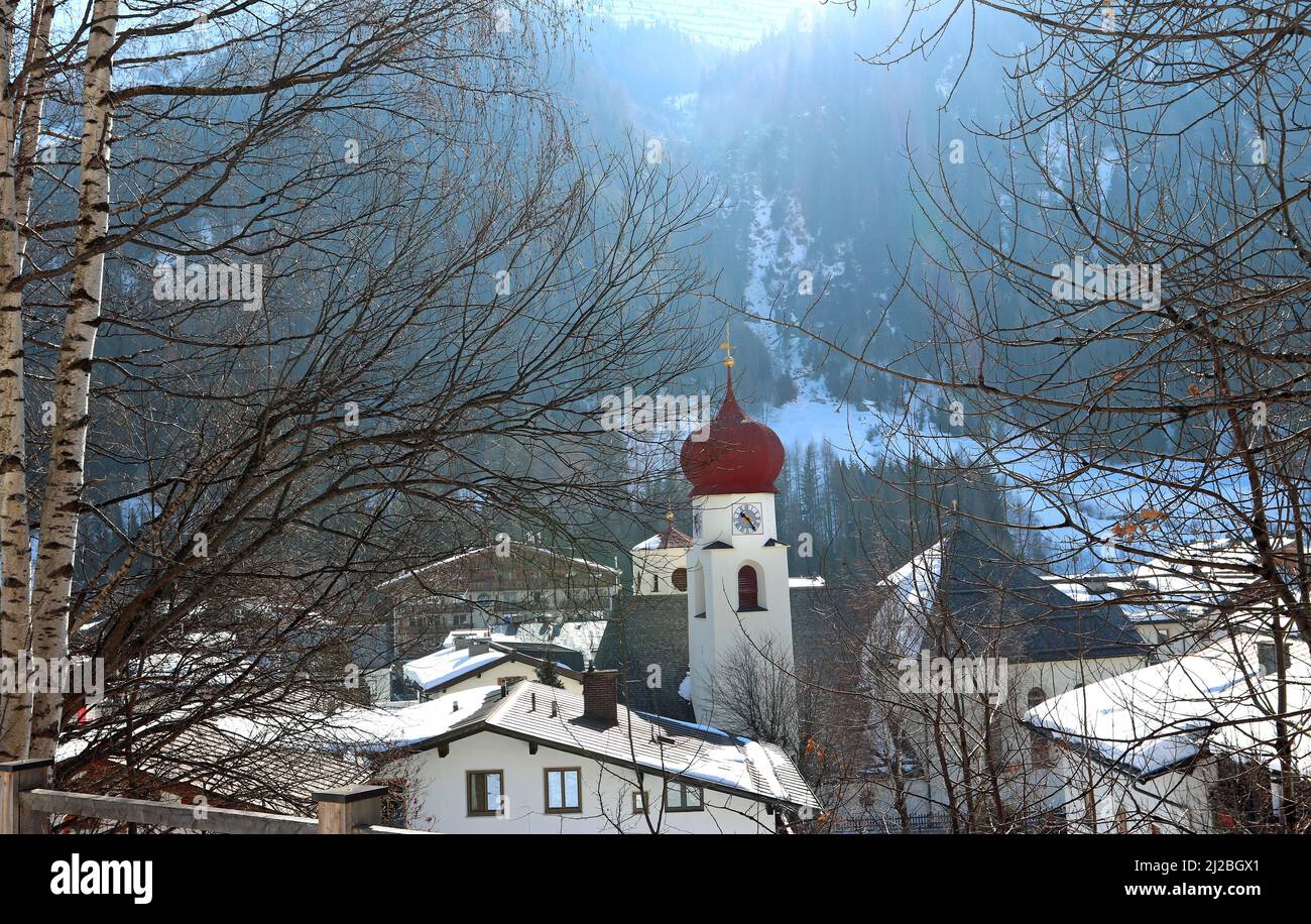 La chiesa parrocchiale a cupola di cipolla nella valle di St Anton am Arlberg: Incorniciata da ornamenti d'argento e tetti innevati, il sole mattutino si riversa sulla montagna. Foto Stock