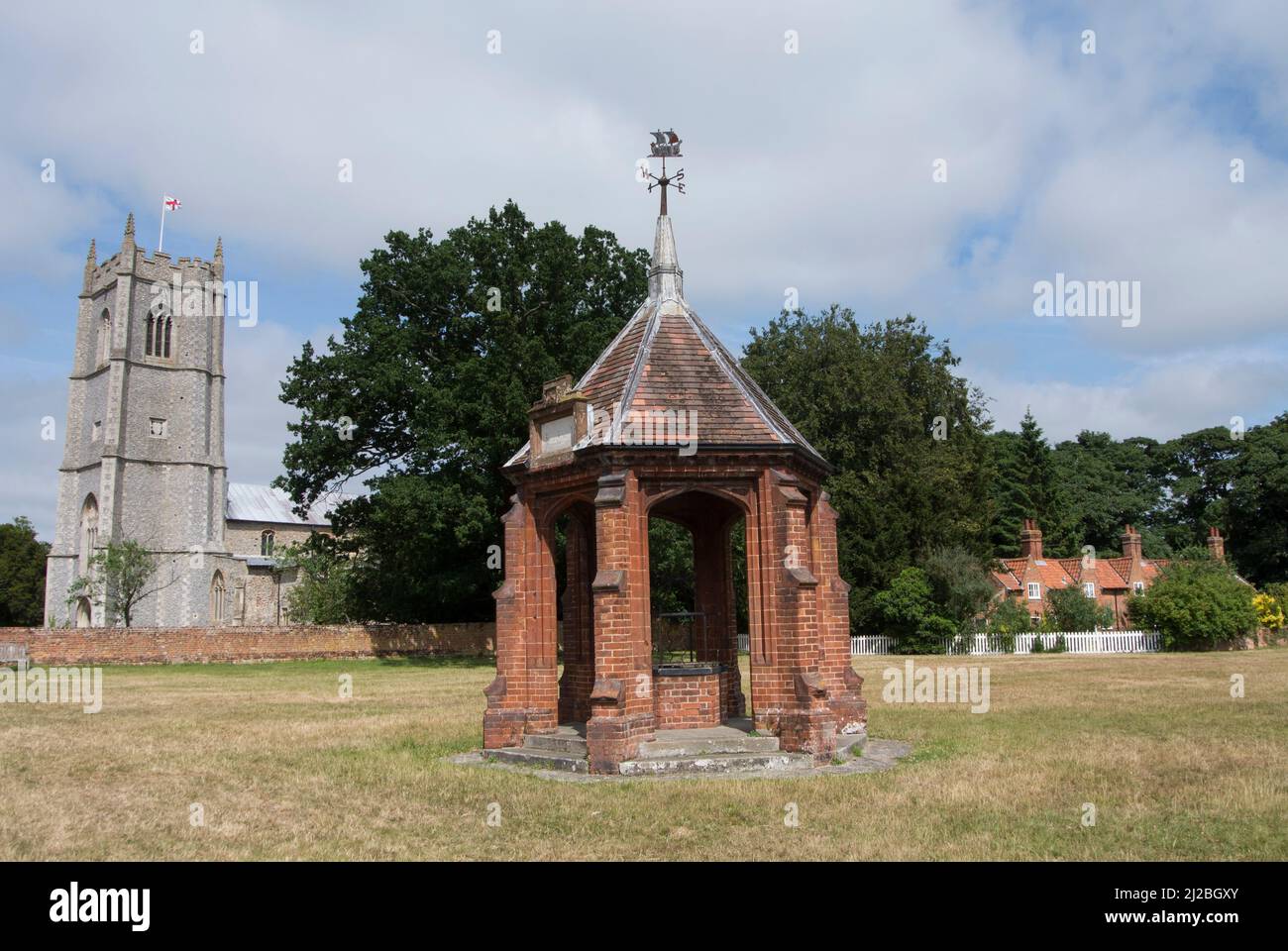 Veduta della chiesa di San Pietro e di San Paolo, la coperta pompa del villaggio e alms case, Heydon Village, Norfolk, Inghilterra Foto Stock