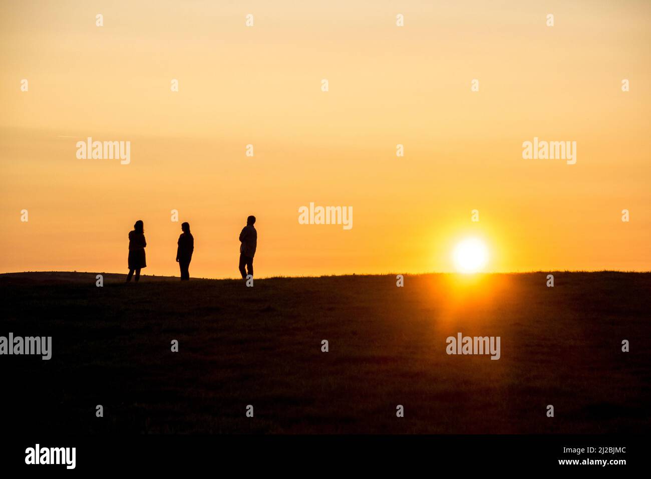Regno Unito, Inghilterra, Devonshire. Un gruppo di persone che guardano il tramonto dalla cima di una collina. Foto Stock