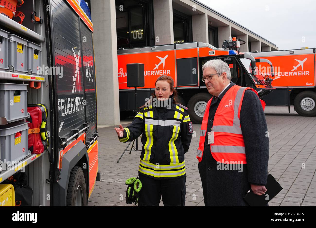 31 marzo 2022, Berlino, Schönefeld: Annika Bogdain, tirocinante presso il Dipartimento dei vigili del fuoco dell'aeroporto di Berlino Brandeburgo "Willy Brandt", spiega un veicolo di gruppo antincendio ausiliario (HLF) a Jörg Steinbach (SPD), ministro dell'economia, del lavoro e dell'energia di Brandeburgo, durante un evento stampa per segnare l'inizio della formazione presso il dipartimento dei vigili del fuoco dell'aeroporto. Il veicolo differisce da un normale camion dei pompieri per il fatto che dispone di attrezzature più estese per l'assistenza tecnica. A partire da agosto 2022, il reparto antincendio del sito BER offrirà corsi di formazione per i vigili del fuoco. All'inizio devono essere occupate sei posizioni apprendisti. P Foto Stock