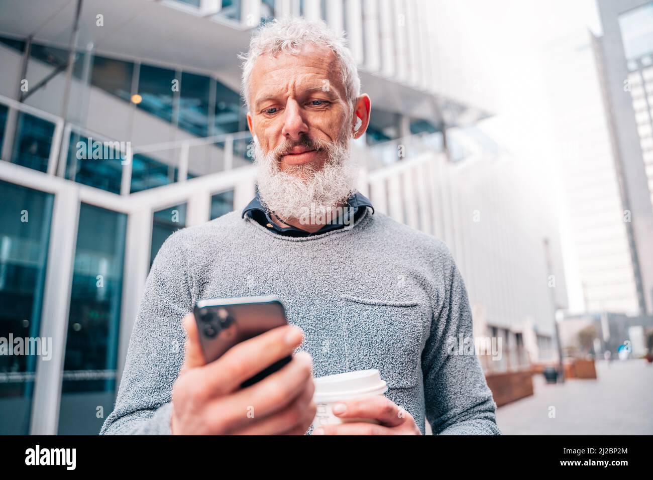 Un uomo d'affari fuori dall'ufficio legge le e-mail dallo smartphone Foto Stock