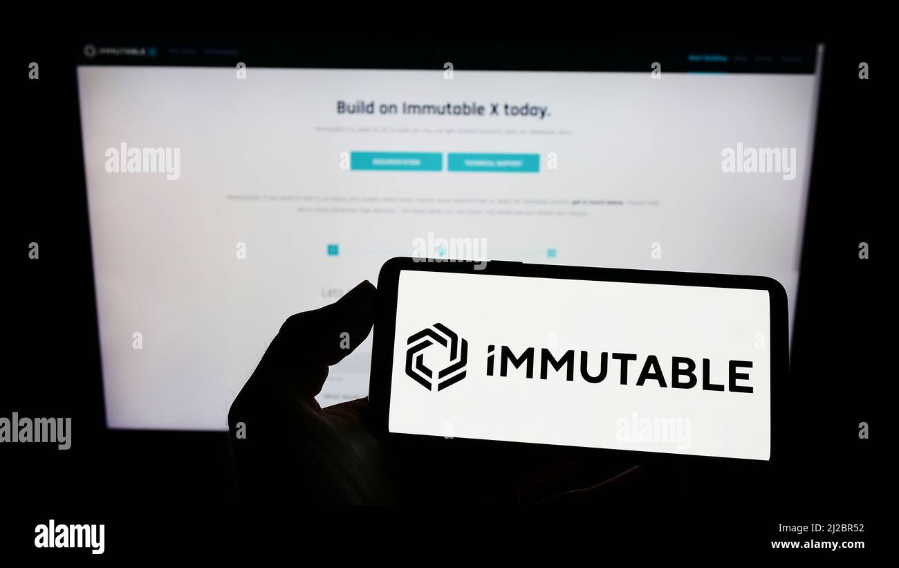 Persona che tiene il cellulare con il logo della società australiana di blockchain Immutable Pty. Ltd. Sullo schermo di fronte al sito web. Mettere a fuoco sul display del telefono. Foto Stock