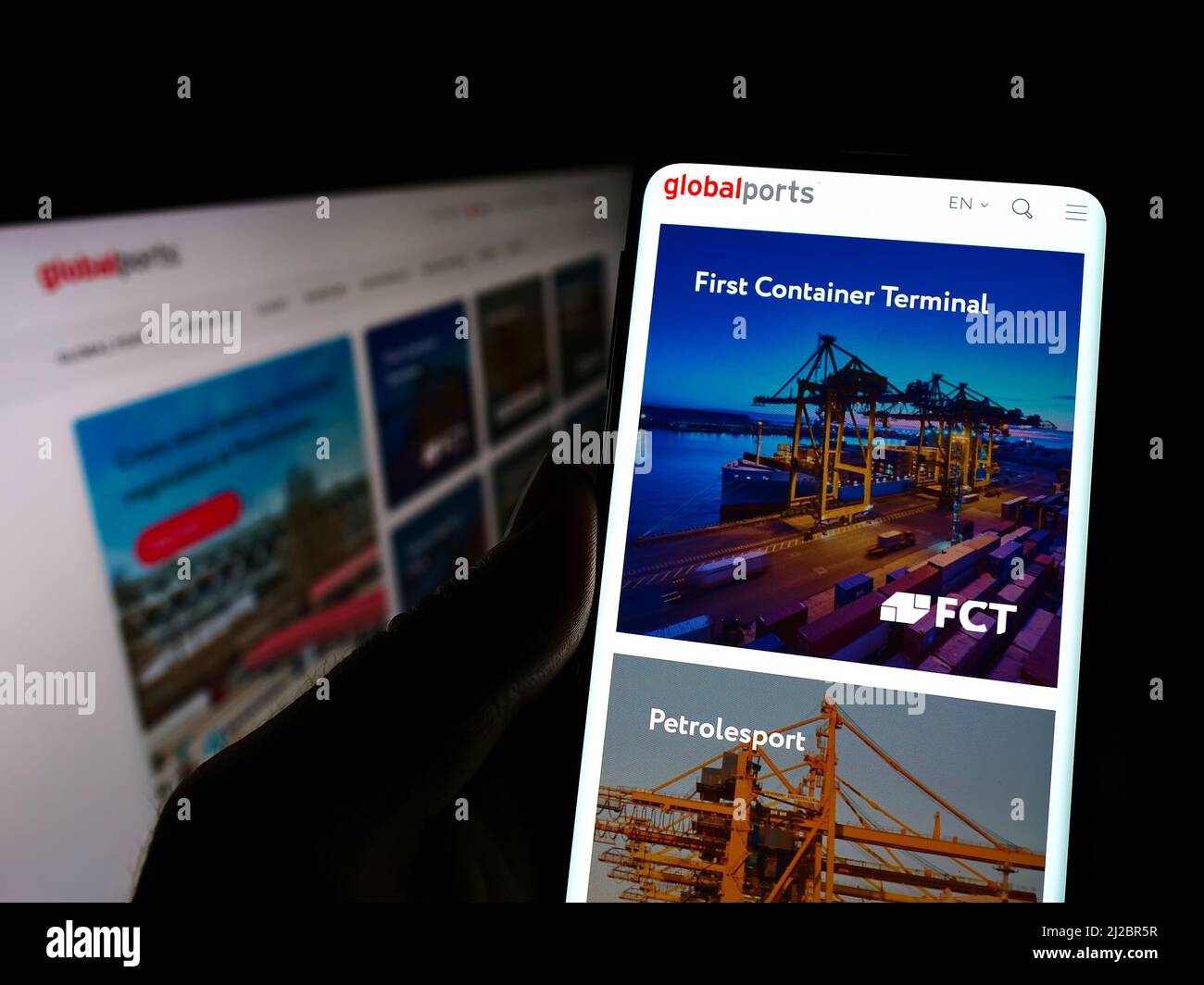 Persona che detiene il cellulare con il sito web della società Global Ports Investments (GPI) sullo schermo di fronte al monitor. Concentrarsi sul centro del display del telefono. Foto Stock