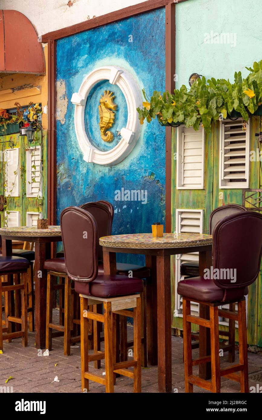 Opere d'arte di un cavallo d'oro in un cerchio bianco sulla parete dietro i tavoli e sgabelli bar di un accogliente bar a Willemstad, Curacao Foto Stock