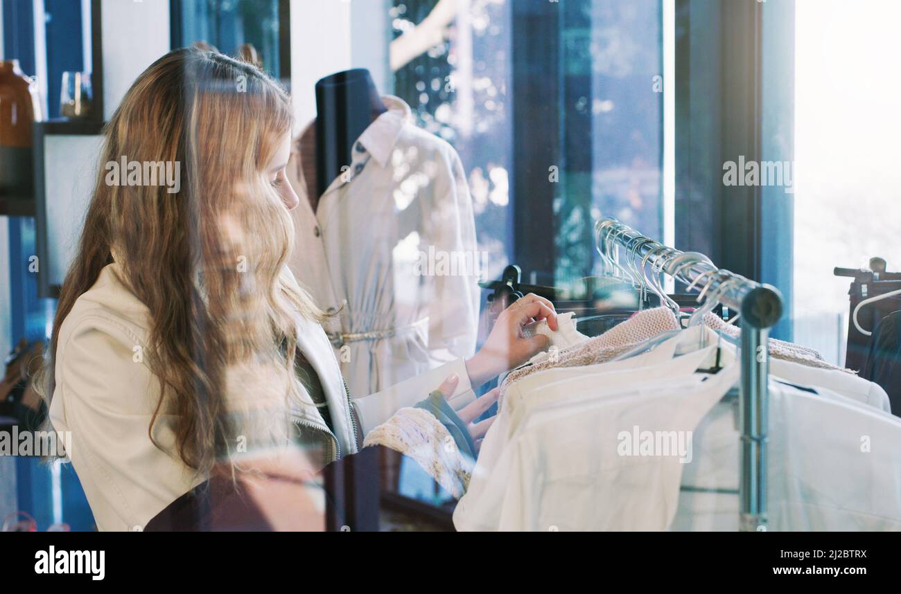 Fai shopping fino a che non si lascia. Scatto di una giovane donna che naviga attraverso i vestiti in una boutique. Foto Stock