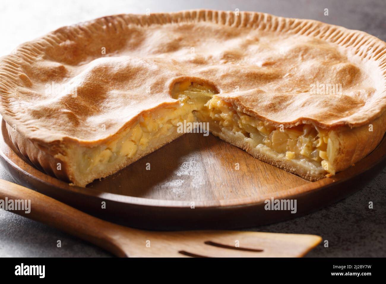Torta di pasta frolla rustica con formaggio e cipolla da vicino in un piatto sul tavolo. Orizzontale Foto Stock