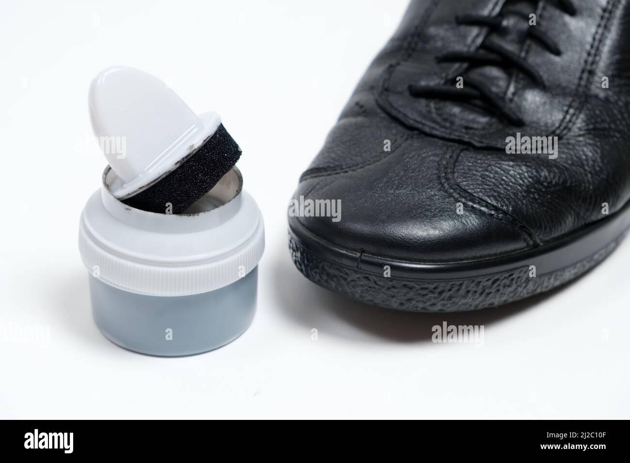 Crema per calzature con spugna e scarpe nere in pelle da uomo su sfondo bianco. Cura delle scarpe Foto Stock