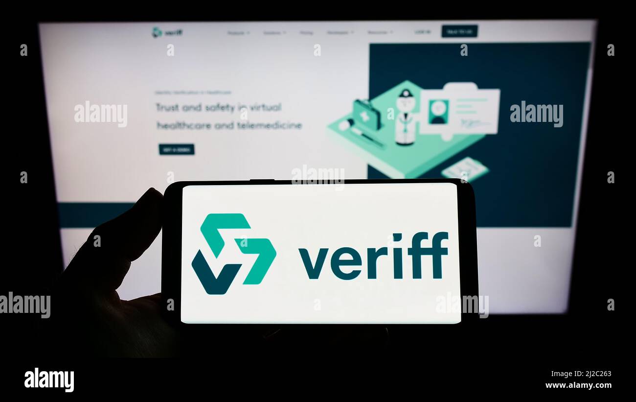Persona che tiene uno smartphone con il logo della società estone di verifica dell'identità Veriff sullo schermo di fronte al sito web. Mettere a fuoco sul display del telefono. Foto Stock
