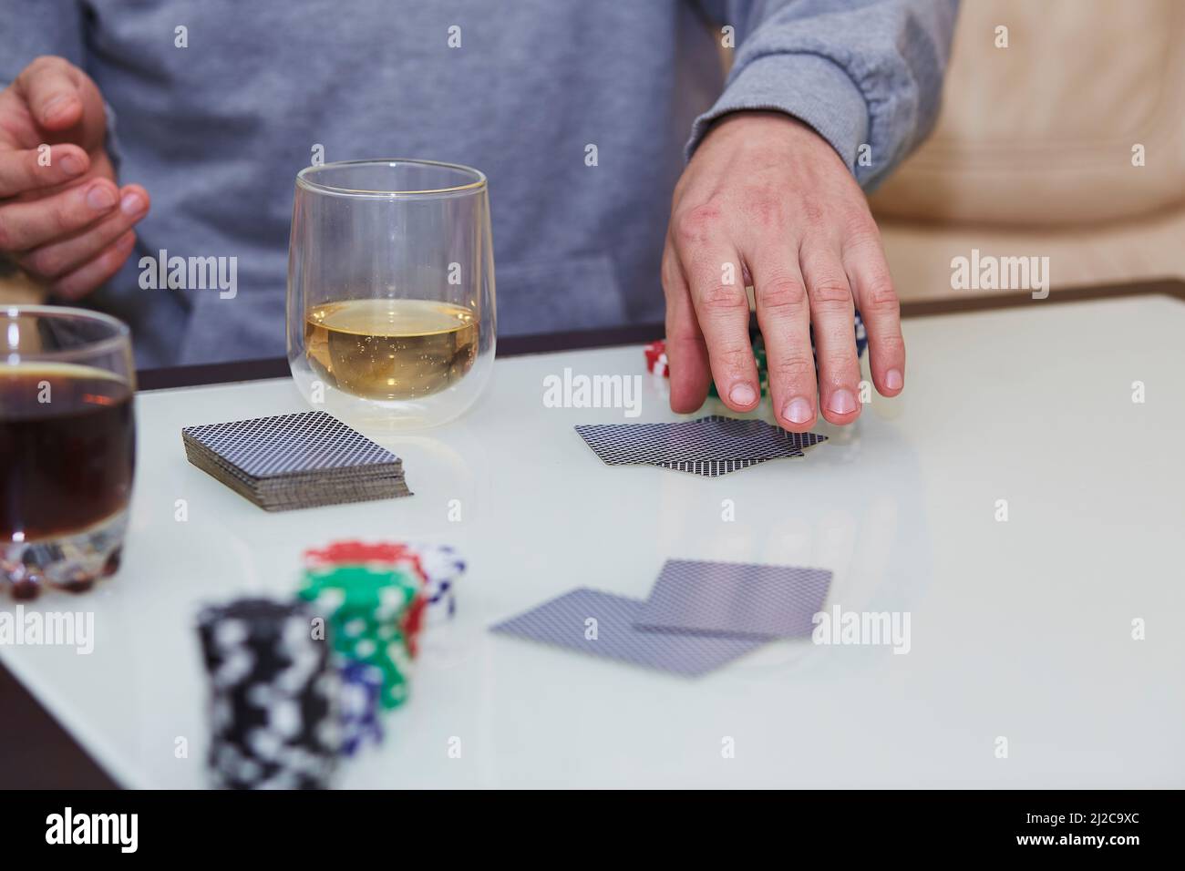 Carte shuffle mani uomo. Gioco di poker con chip, carte sul tavolo. Bicchiere di whiskey. Godendo il momento, detox digitale con gli amici. Fotografia di stile di vita. Momento candida. Messa a fuoco selettiva Foto Stock