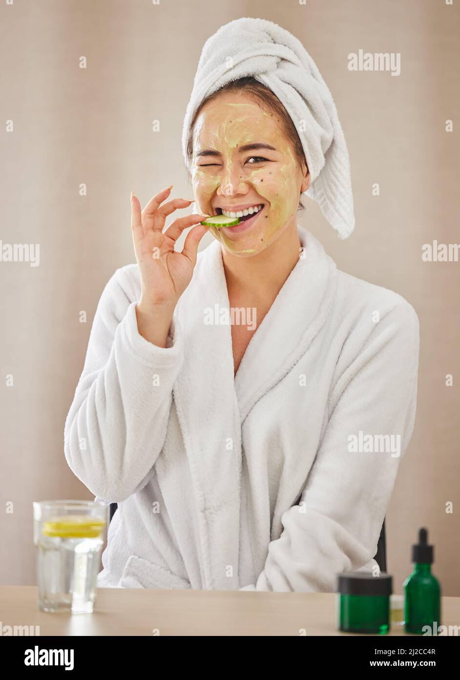 Un tipo di self-care di fine settimana. Shot di una giovane donna che mangia un cetriolo mentre fa un trattamento di bellezza facciale a casa. Foto Stock