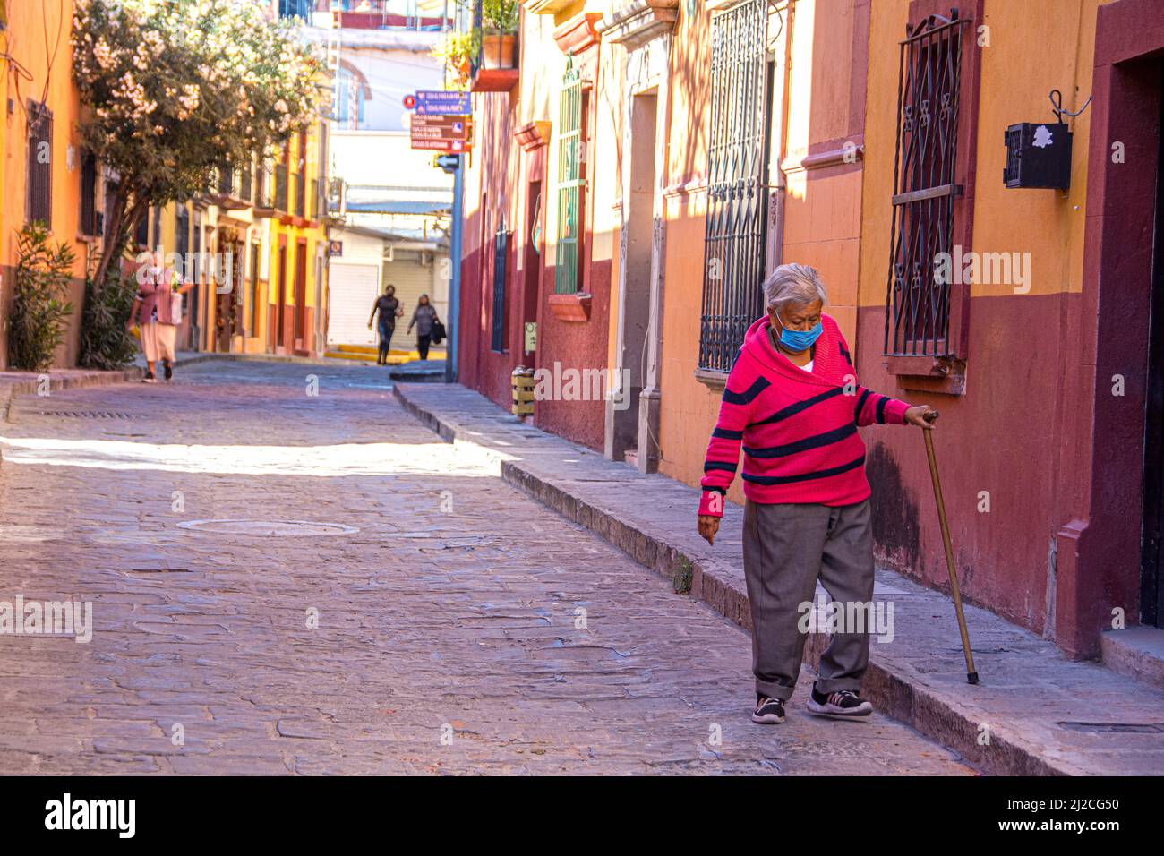Una vecchia donna messicana cammina lungo la strada utilizzando una canna per mantenere il suo equilibrio. San Miguel de Allende, Guanajuato, Messico Foto Stock