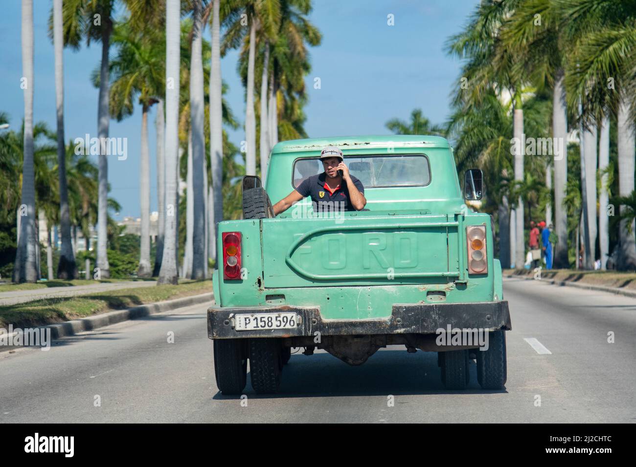 Il giovane uomo cubano corre sul retro di un camion pick up attraverso una strada a l'Avana, Cuba parlando sul suo cellulare. Foto Stock