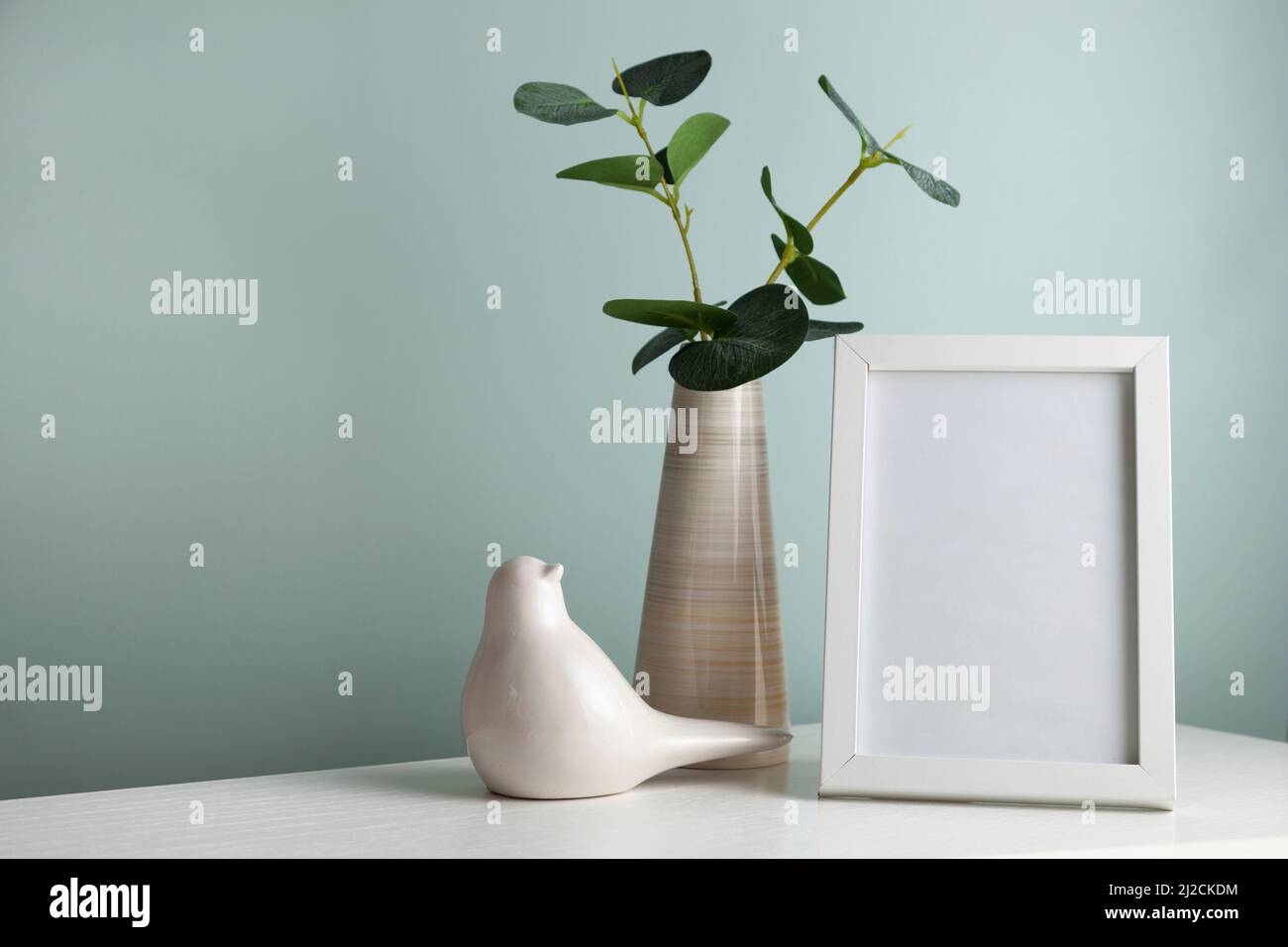 Accogliente tavolo da scrivania con vaso con ramo verde, uccello in ceramica e cornice fotografica. Higge, stile boho, soggiorno scandinavo Foto Stock