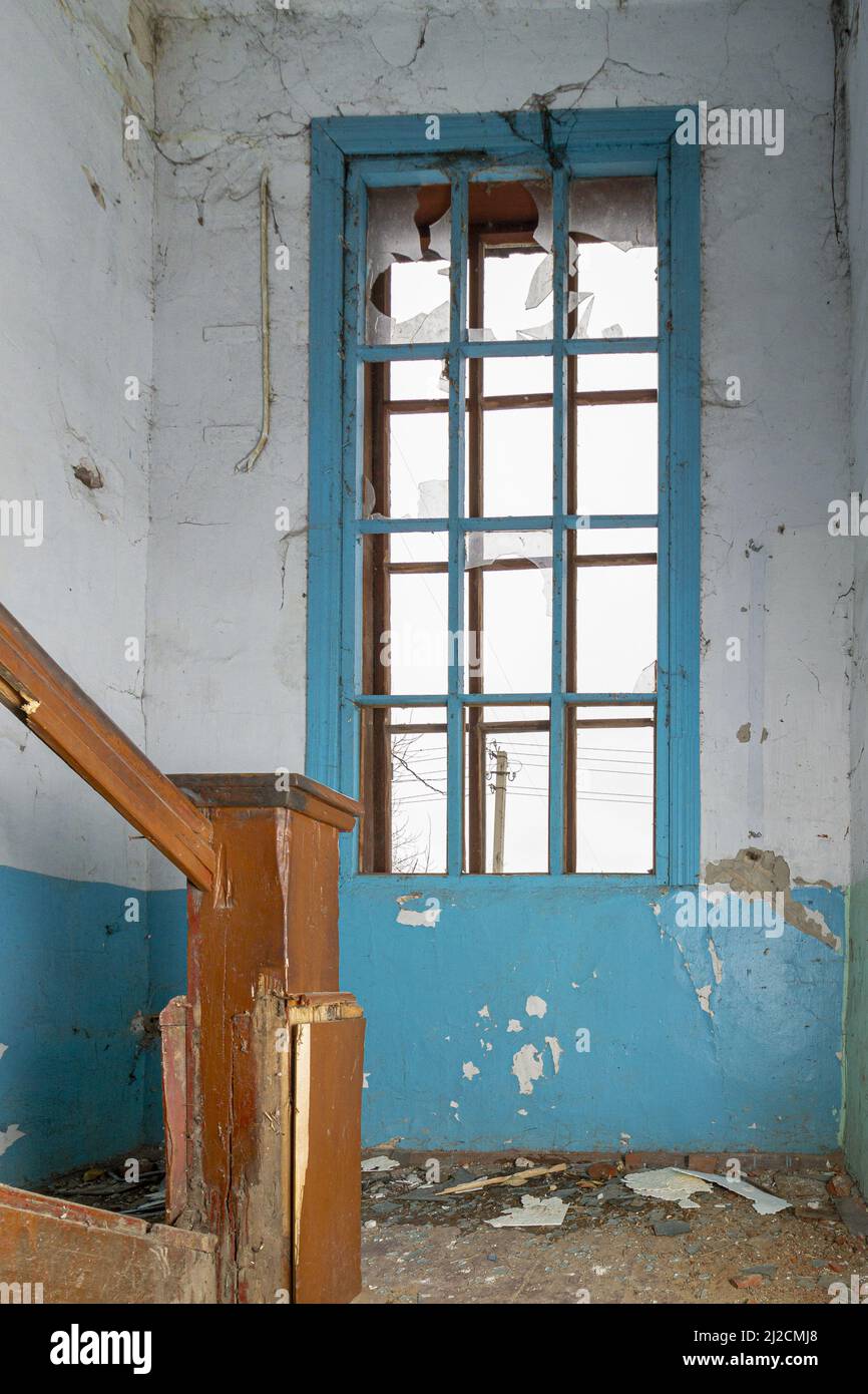 Scala in legno e finestra spezzata della casa abbandonata dai residenti. Distrutta da un edificio residenziale di appartamenti a esplosione. Foto Stock