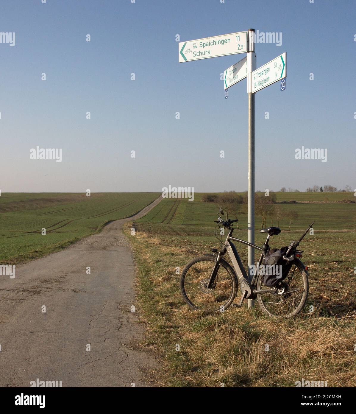 Una bicicletta si trova su un cartello su una pista ciclabile che conduce attraverso campi infiniti nella Germania sudoccidentale. Foto Stock