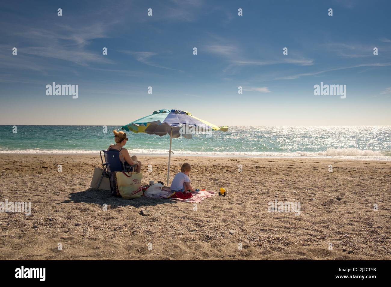 Madre con suo figlio seduto sotto l'ombrello all'ombra in una giornata calda godendo le vacanze estive nel mar Egeo Foto Stock