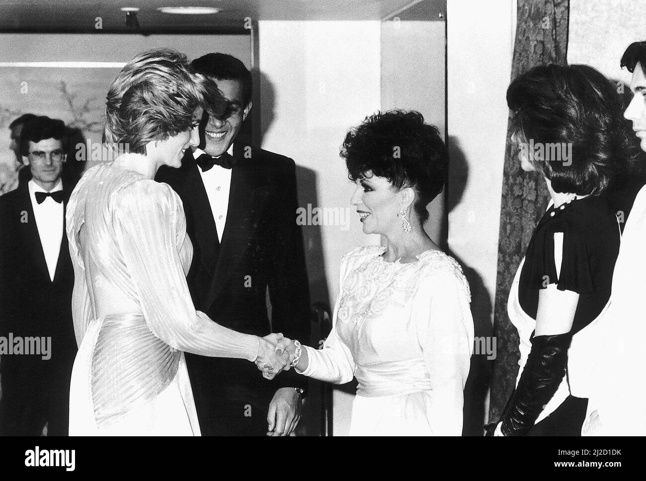 La principessa Diana scrolla le mani con l'attrice Joan Collins ad un Soiree di moda di Bruce Oldfield London tenuto a Grosvenor House a Londra in aiuto della carità Barnardos, di cui è appena diventata presidente e dove il progettista è stato portato up.The Princess sta portando un pleated, aperto indietro, Odeon drappeggiato di raggi solari in argento e oro zoppo, progettato da Bruce Oldfield. 26th marzo 1985. Foto Stock