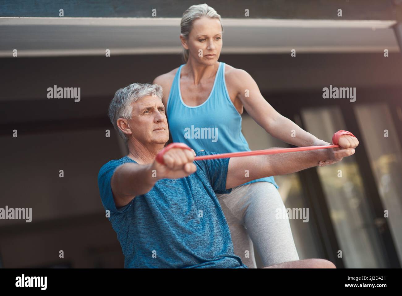 Centratevi e potete fare qualsiasi cosa. Colpo di un uomo maturo che allunga i muscoli del braccio con una fascia elastica mentre è assistito da una donna. Foto Stock