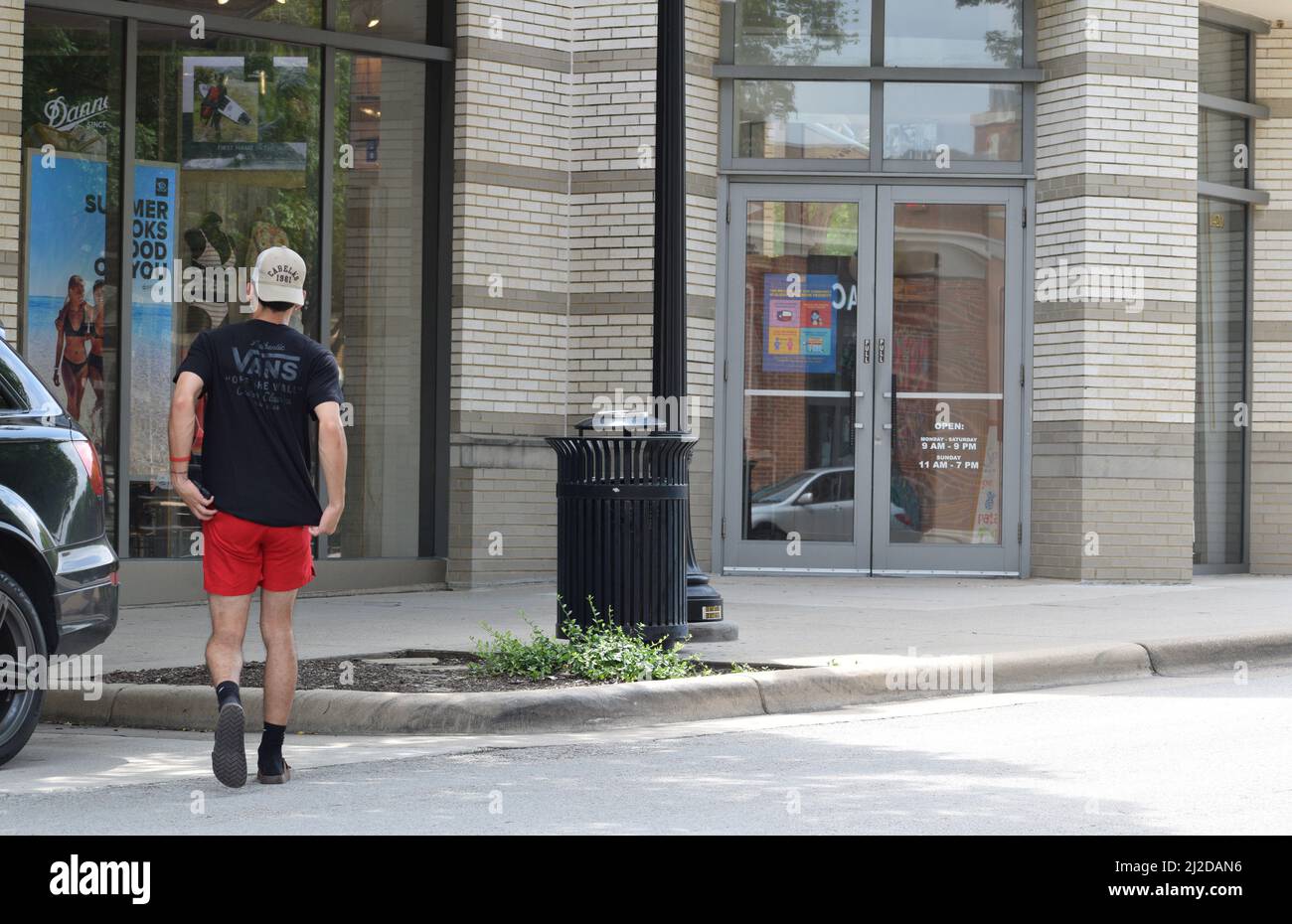 Gen Z uomo in pantaloncini rossi e maglietta nera a piedi in un negozio a Southlake Town Square; Southlake, Texas Foto Stock