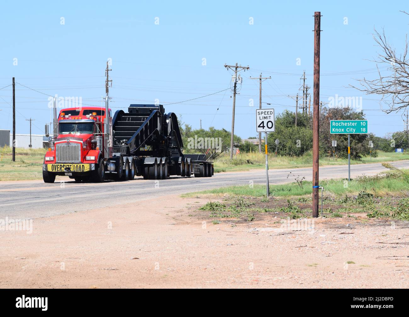 Semi-camion rosso che tira un carico sovradimensionato lungo un'autostrada a Rule Texas - Agosto 2021 Foto Stock