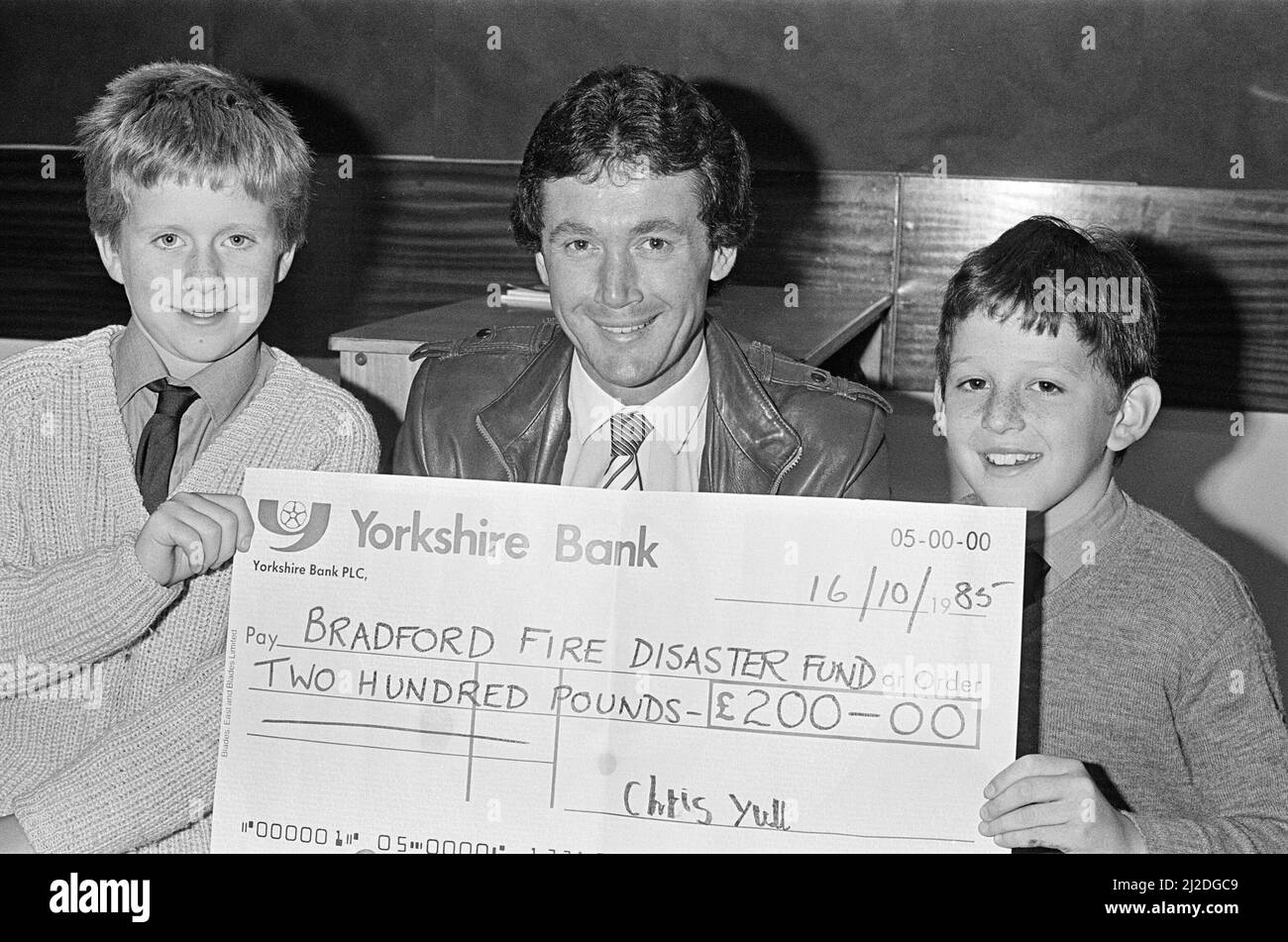 Trevor Cherry, ex calciatore di Huddersfield che vive a Lepton, è responsabile del calcio di Bradford City, con un assegno del £200 per il fondo contro i disastri antincendio degli alunni della Lepton Middle School Matthew Holroyd (a sinistra) e Chris Yull, entrambi 10. I due ragazzi hanno raccolto i soldi facendo una corsa sponsorizzata di 18 giri intorno al terreno di Huddersfield Town. 16th ottobre 1985. Foto Stock