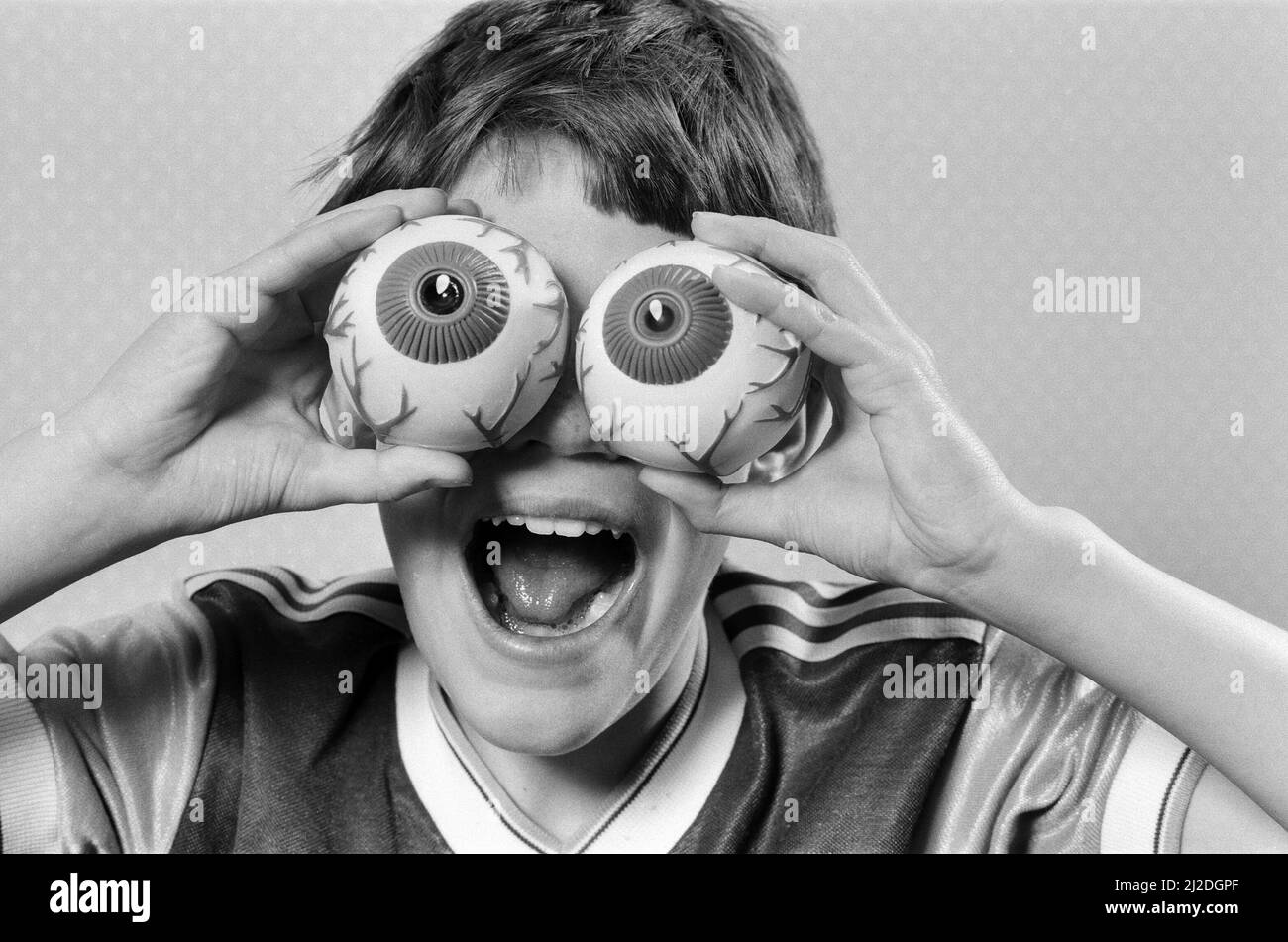 Un ragazzo giovane che tiene i giocattoli falsi della sfera dell'occhio fino ai suoi occhi. 21st ottobre 1986. Foto Stock