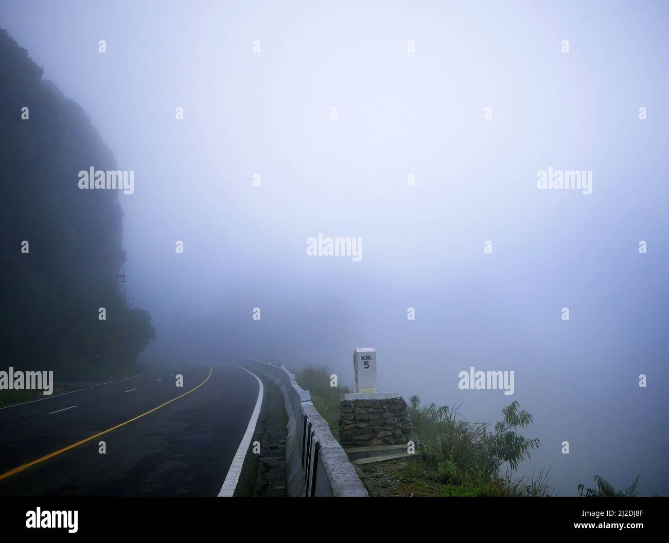 Strada asfaltata con linea gialla in cima alla montagna nella nebbia mattutina Foto Stock