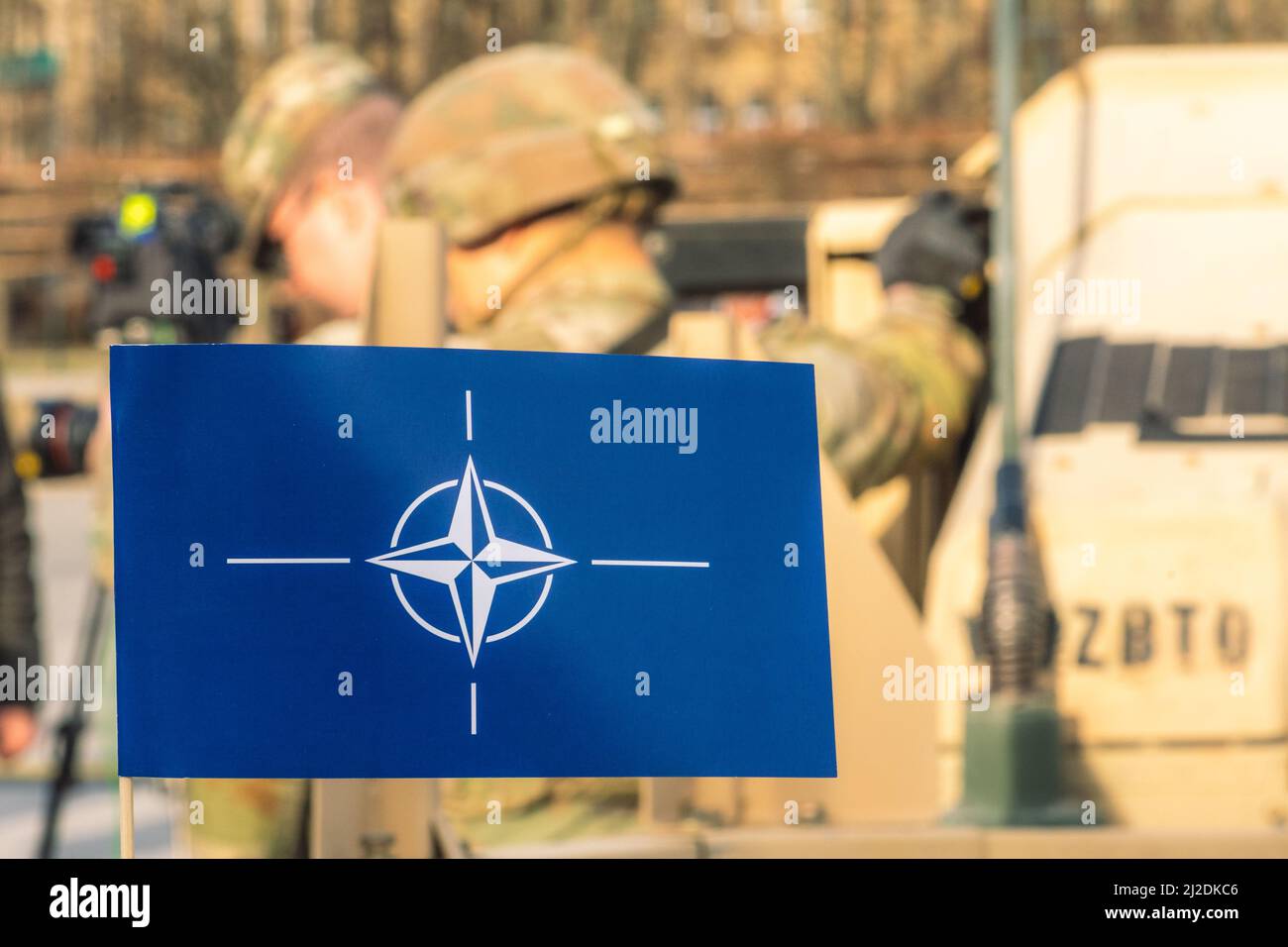 Bandiera e simbolo della NATO, Organizzazione del Trattato del Nord Atlantico, unità di integrazione della forza con soldati fuori fuoco con caschi e veicoli militari Foto Stock