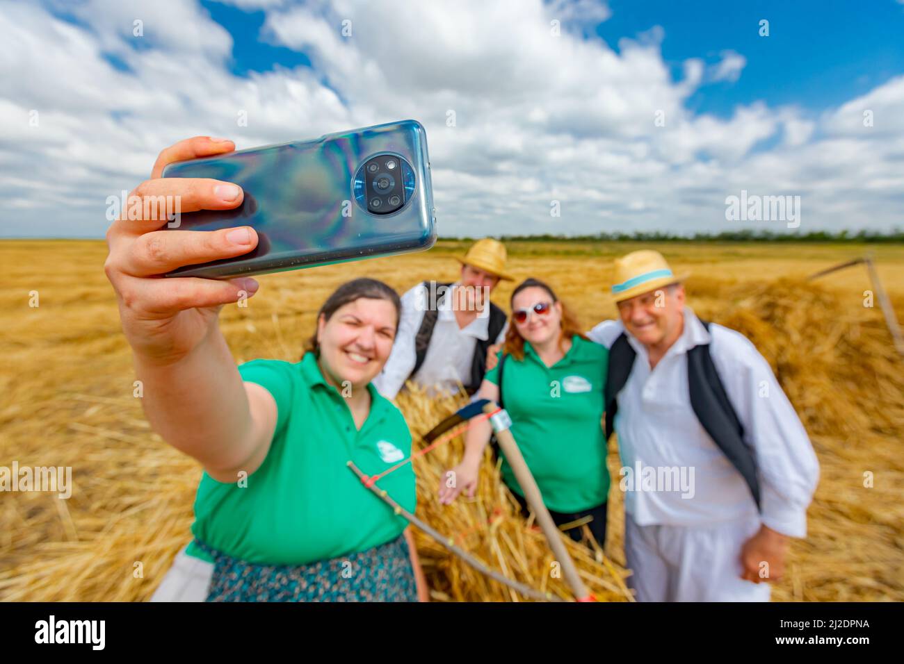 Muzlja, Vojvodina, Serbia, - 03 luglio 2021; XXXVIII tradizionalmente raccolto di grano. Donna prende selfie con i suoi amici dopo il raccolto, una foto in più per Foto Stock