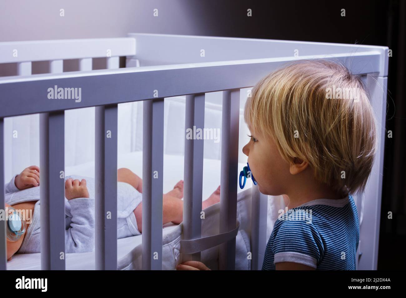 Il fratello del ragazzo del toddler osserva nella greppia della sorella neonata Foto Stock