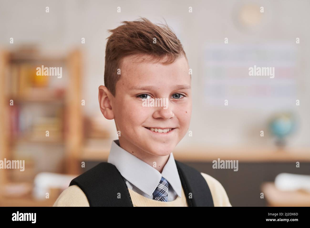Primo piano ritratto di ragazzo sorridente a scuola guardando la macchina fotografica mentre si trova in aula, spazio copia Foto Stock