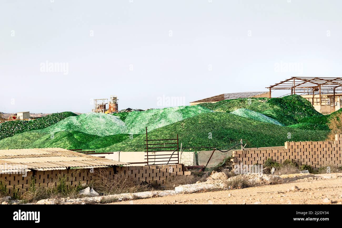 cumuli di bottiglie di vetro riciclate verdi e trasparenti, frantumate e rotte in attesa di essere utilizzate in una vetreria con un cielo blu pallido sfondo Foto Stock