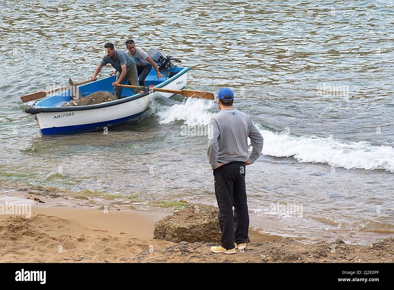 I pescatori che si trovano all'interno di una barca che tiene le pale che escono dall'acqua, piene di pesci intrappolati nella rete da pesca. Un uomo che li guarda. Foto Stock