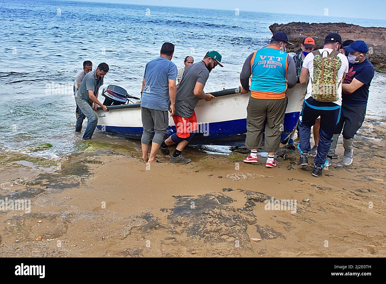 Un gruppo che aiuta i pescatori a sollevare una barca dall'acqua. Gilet del club VTT. Nome della nave Camilia in arabo. Spiaggia di Ain Defla, Gdyel, Cap d’Aiguille. Arzew. Foto Stock