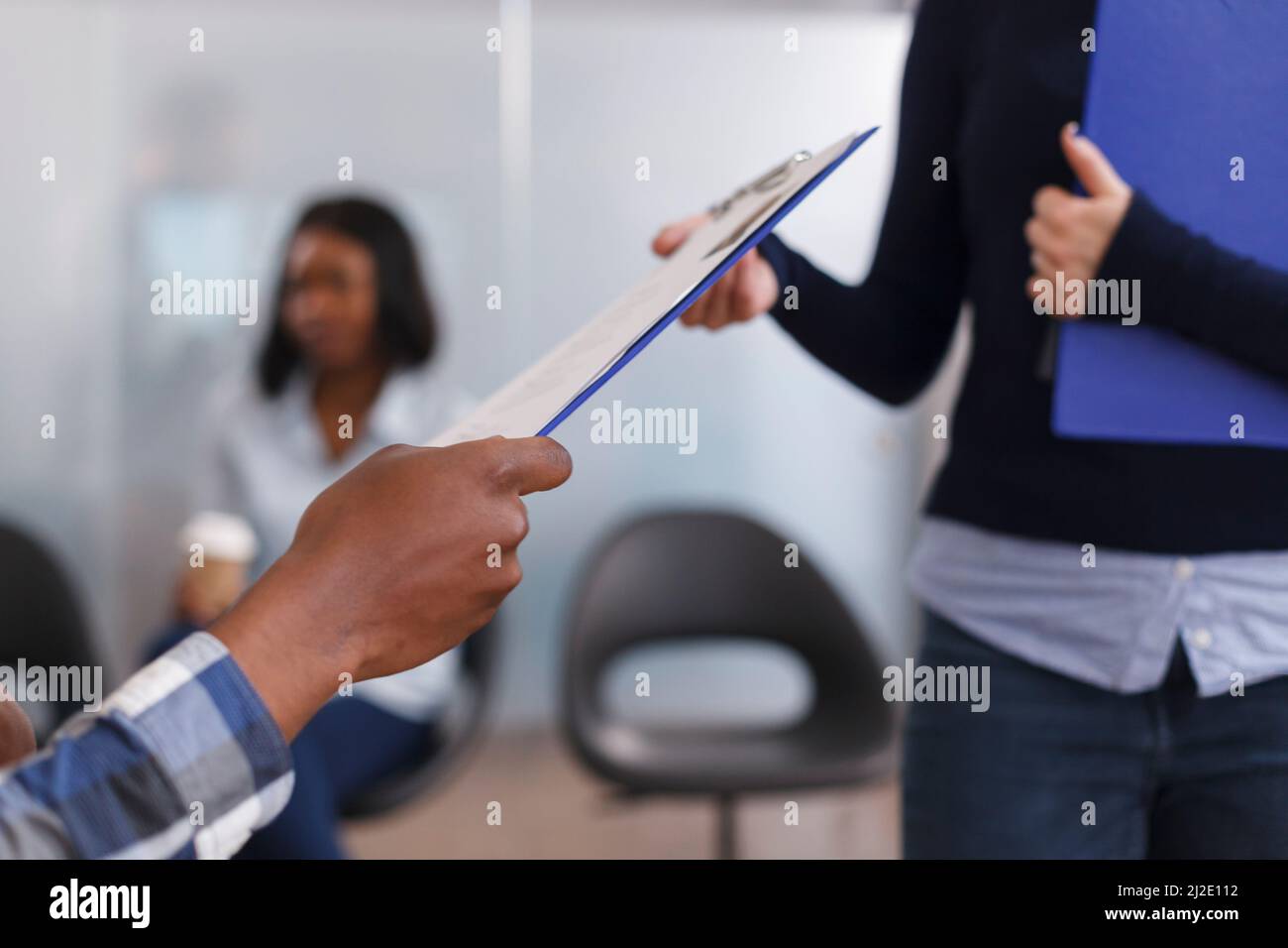 Primo piano delle mani dell'uomo afroamericano che danno il CV del responsabile del reparto di occupazione e la domanda di lavoro mentre nell'area della lobby. Donna d'affari che riceve gli appunti del candidato con i documenti. Foto Stock