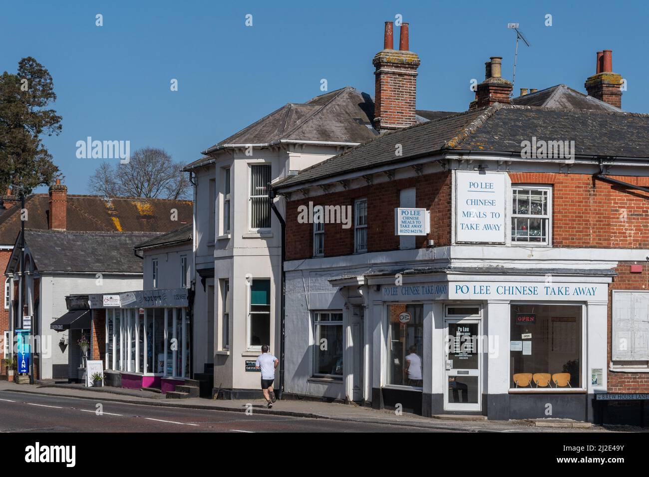Hartley Wintney Village, Hampshire, Inghilterra, Regno Unito. Vista delle aziende sulla High Street con un pareggiatore in esecuzione Foto Stock