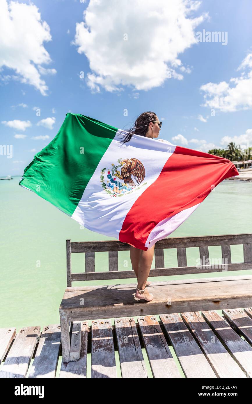 La donna tiene dietro la sua schiena la bandiera messicana mentre si trova su una panchina su un molo vicino al Mar dei Caraibi. Foto Stock