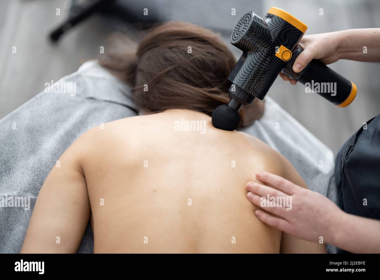 La donna massaggia la schiena del paziente con un massaggiatore a percussione Foto Stock