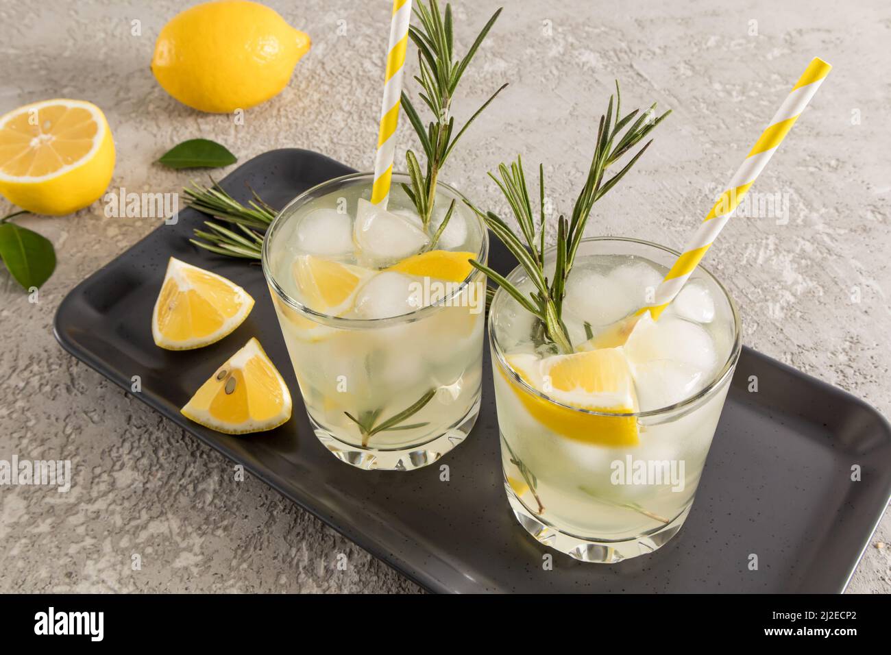 due bicchieri d'acqua di vitamina di agrumi su un vassoio di ceramica scuro con fette di limone e rosmarino. detox acqua Foto Stock