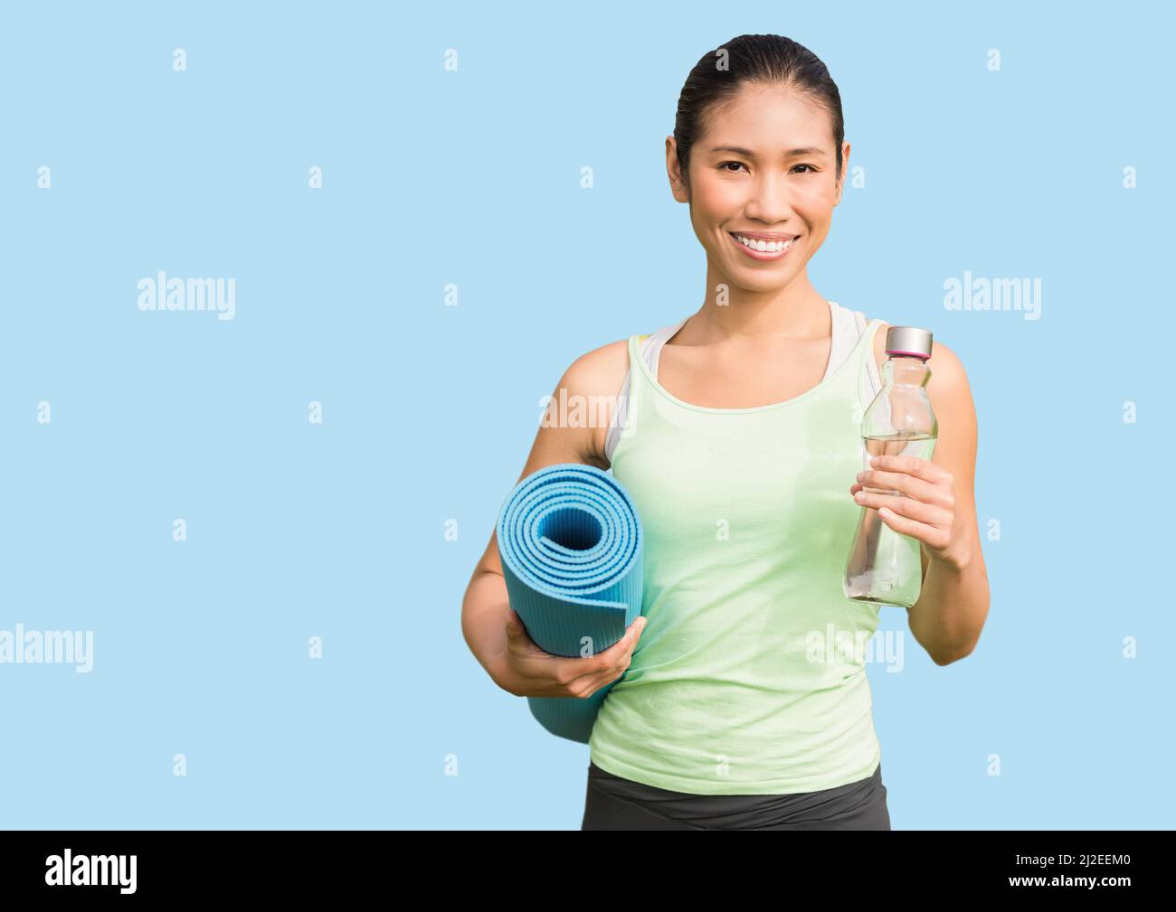 Donna asiatica in forma che tiene una bottiglia d'acqua e un tappetino yoga sorridendo sullo spazio copia su sfondo blu Foto Stock