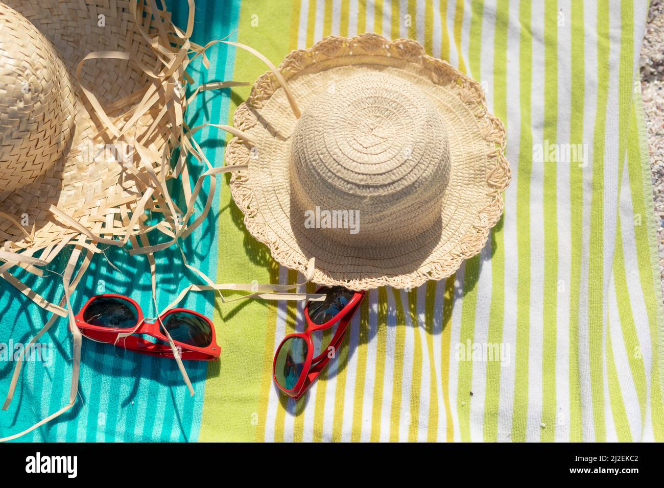 Vista ad alto angolo di cappelli da sole e occhiali da sole su un asciugamano in spiaggia durante la giornata di sole Foto Stock