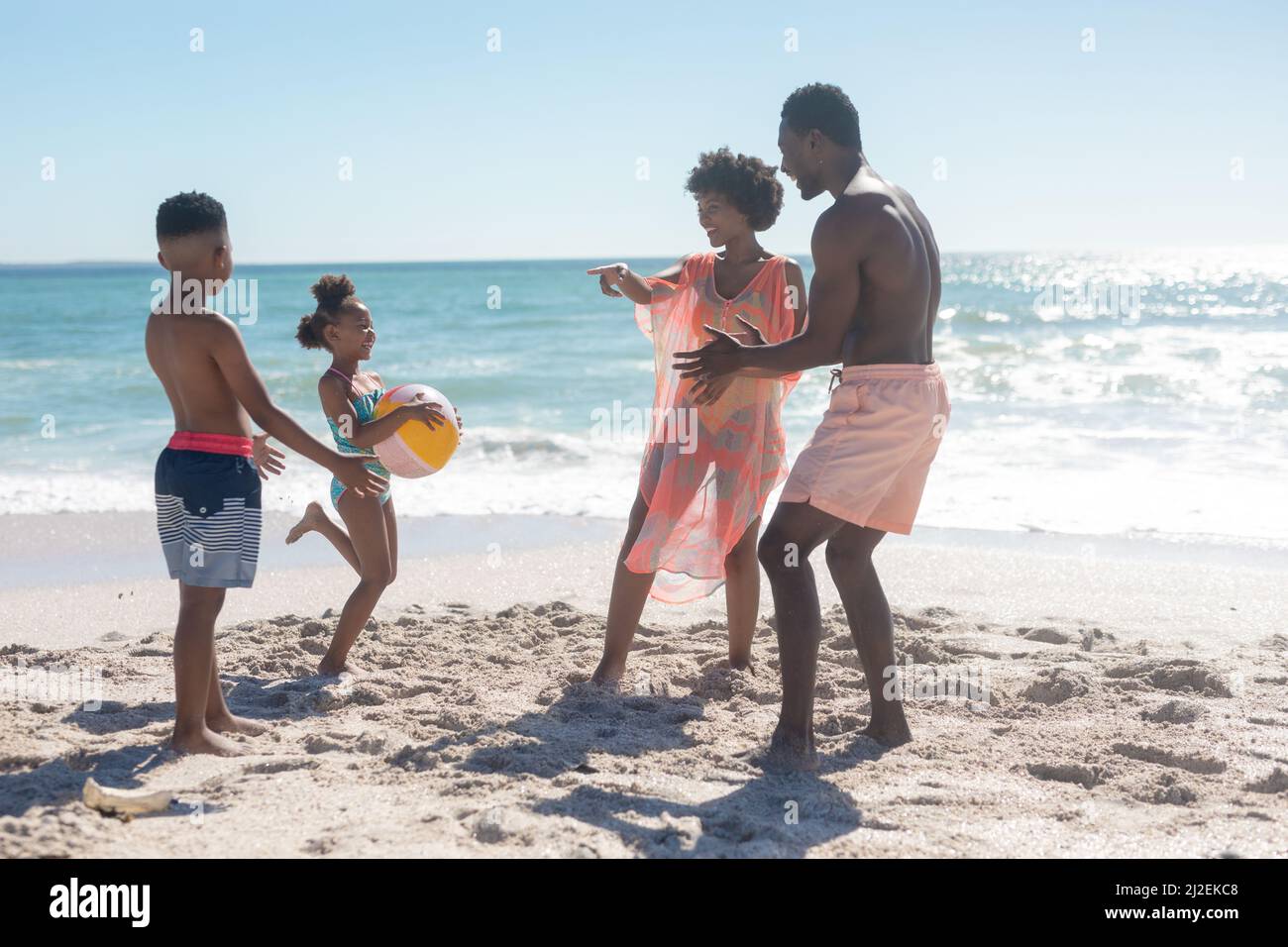 Tutta la durata della famiglia afro-americana felice che gioca con la palla in spiaggia in giorno di sole Foto Stock